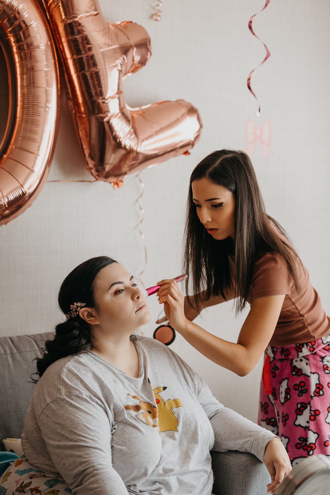 Chelsie sitting while makeup is applied beside rose gold bride balloons