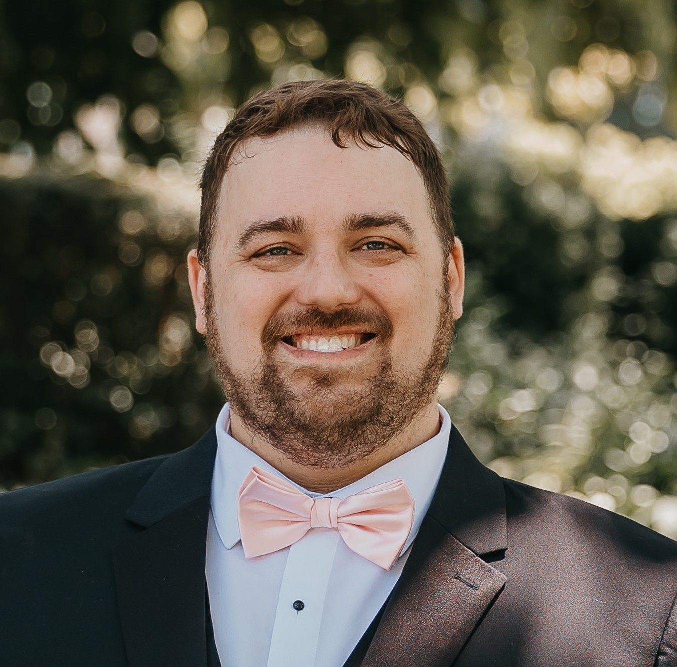 Greg smiling in a suit with a blush bow tie
